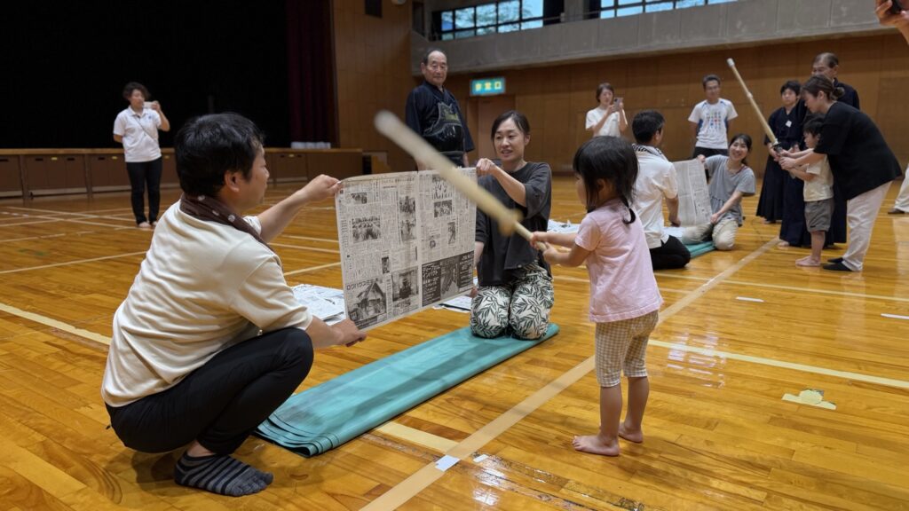 竹刀で新聞紙を切る子どもと、新聞を持つ大人